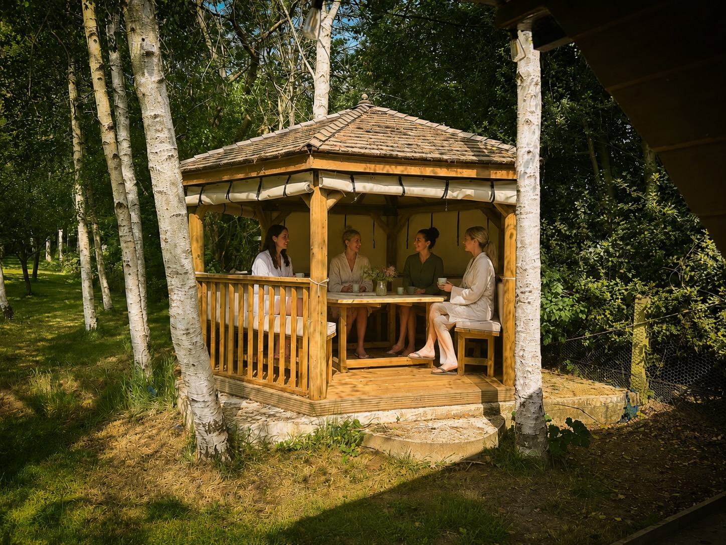 Guests relaxing together in the wooden gazebo among silver birch trees