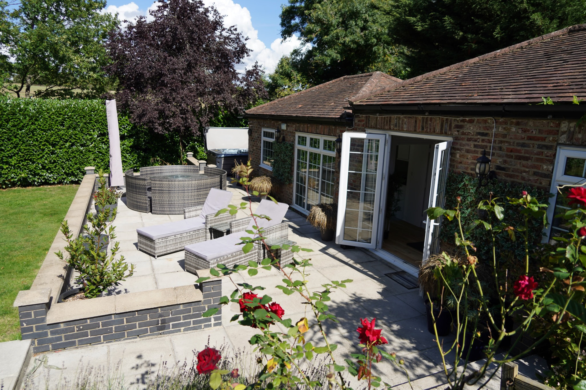 Sun-lit patio with hot tub, loungers and roses outside the wellness centre